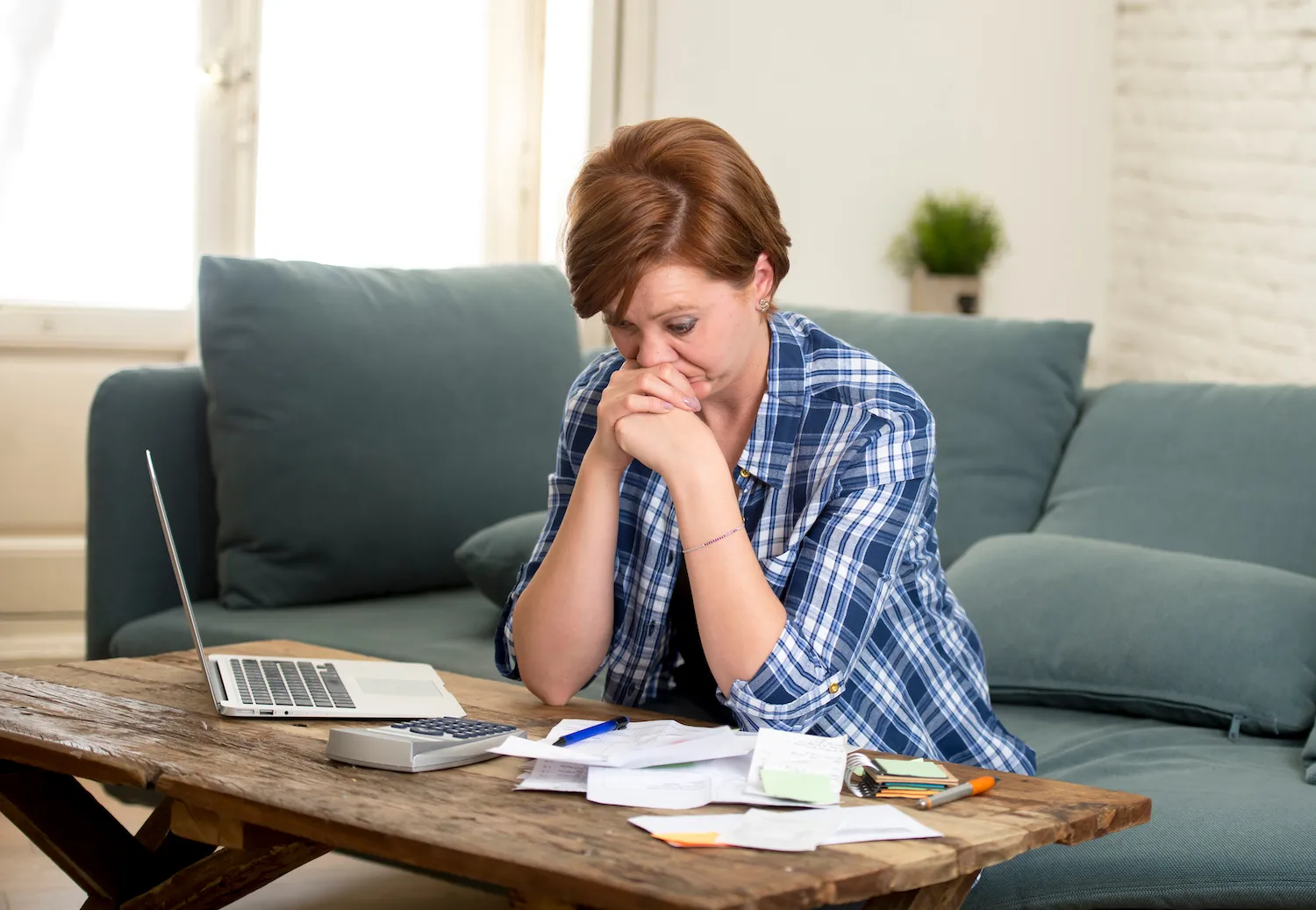 Woman sitting in front of her laptop looking at all her overdue bills next to her